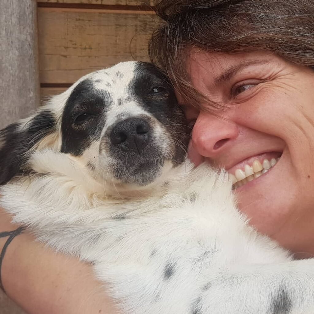 Carolina abraçada com a cachorrinha Chica no Acãochego, em ambiente familiar.